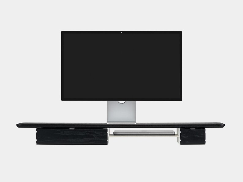 May include: A black wooden monitor stand with two drawers and a shelf for a laptop. The stand supports a large computer monitor with a silver base. The design is modern and minimalist.