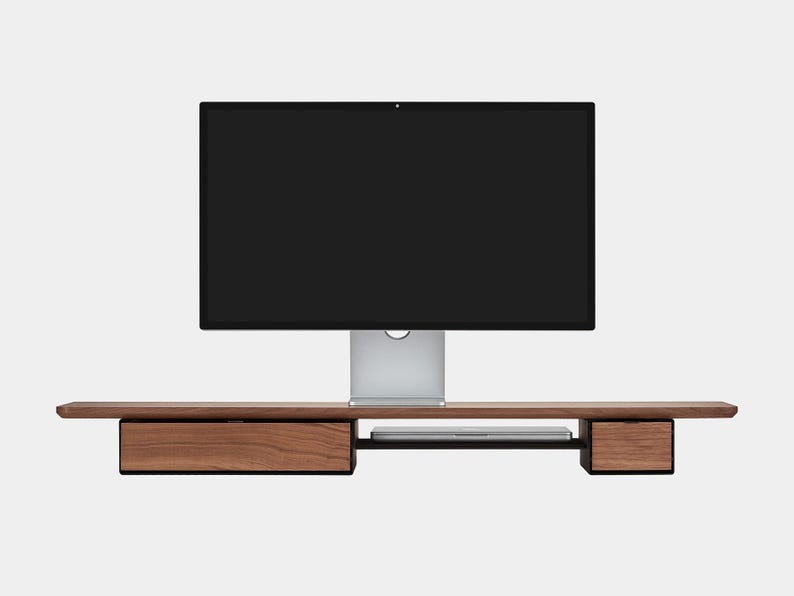 May include: A modern wooden monitor stand with two drawers and a shelf for a laptop. The stand is made of dark wood and has a sleek, minimalist design. A large black computer monitor sits on top of the stand.