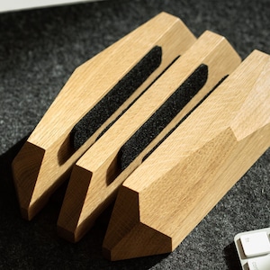 May include: Three wooden phone stands with black felt lining the grooves. The stands are stacked on top of each other and are made of light brown wood.