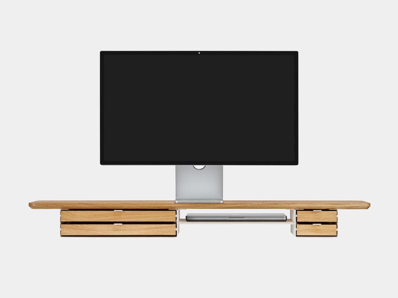 May include: A wooden computer monitor stand with a built-in shelf and drawers. The stand supports a large black screen monitor. The stand has two sets of drawers on either side and a shelf for a laptop.
