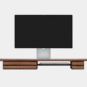 May include: A modern wooden desk with two drawers on each side and a central shelf. A large computer monitor sits on top. The desk is made of dark wood and has a minimalist design.