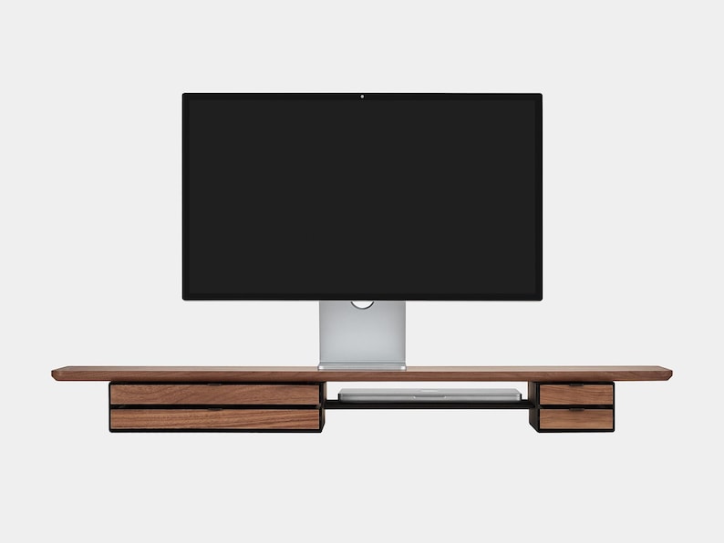 May include: A modern wooden desk with two drawers on each side and a central shelf. A large computer monitor sits on top. The desk is made of dark wood and has a minimalist design.