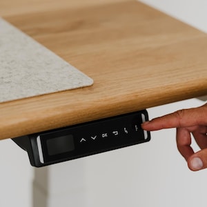 May include: A black control panel with a digital display and buttons for an adjustable standing desk. The buttons include up, down, OK, and memory presets.