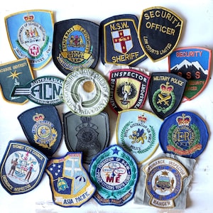 May include: A selection of embroidered patches featuring diverse designs and text. Patches include "Security Officer," "Sheriff," "Military Police," and "Australian Customs." The patches are in various shapes and colours, with detailed stitching.