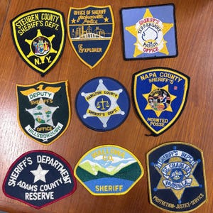 May include: A collection of nine embroidered law enforcement patches in various shapes and colours. The patches feature text including Steuben County Sheriff's Dept, Jacksonville Police Explorer, Terrebonne Parish, Hillsborough Deputy Sheriff, Hamilton County, Napa County Mounted Posse, Adams County Sheriff's Department Reserve, Wallowa Co. Sheriff, and St. Charles Parish Sheriff's Dept.