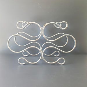 May include: A silver metal wine rack with a decorative, swirling design. The rack holds six bottles of wine.