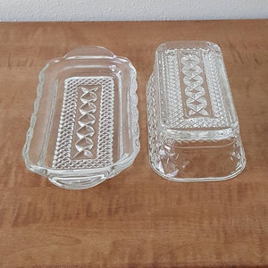 May include: Two clear glass butter dishes with a diamond pattern. The dishes are rectangular and have a raised edge.