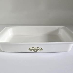 May include: A rectangular, off-white baking dish with a decorative olive-green floral design on the front. The dish has slightly raised sides and is designed for oven use. The overall shape is square.