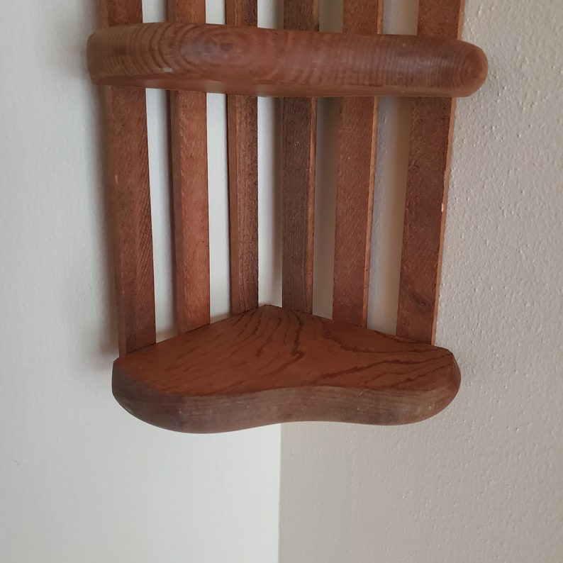 May include: A wooden corner shelf with two shelves. The shelves are made of wood slats and have a rounded edge.
