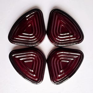 May include: Four triangular, burgundy-colored glass coasters with a ridged interior design and black trim. The coasters are arranged in a square formation against a white background. Each coaster has a unique, geometric shape.
