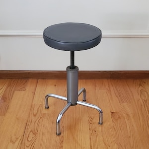 May include: A gray upholstered adjustable stool with a chrome base and four legs.