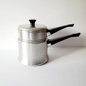May include: A silver double boiler with black handles. The top pot has a lid.