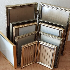 May include: A set of eight gold-toned picture frames of varying sizes. The frames are all made of metal and have a decorative design. The frames are arranged in a stack, with the largest frame at the bottom and the smallest frame at the top.