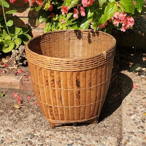 May include: A large, brown, woven bamboo basket with a round top and a wide base. The basket is made of natural materials and has a rustic, handcrafted look.
