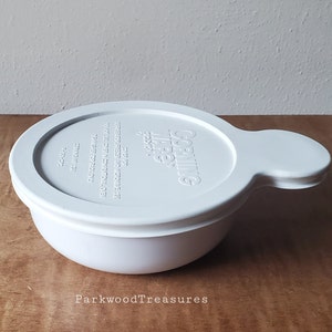 May include: White Corning Ware bowl with a white lid. The lid has a handle and the text "Corning Ware" and "Classic" printed on it.