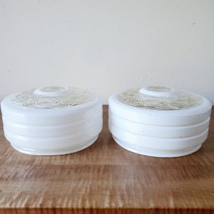 May include: A pair of round, white glass light fixture shades featuring a tiered, ribbed side profile and a clear, textured glass center panel with a circular pattern. Each shade has a central opening for mounting, presenting a clean, uniform look.
