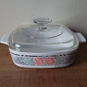 May include: White square baking dish with a glass lid. The dish has a floral design with pink roses and green leaves on a gray background. The text "ParkwoodTreasures" is visible on the bottom of the dish.