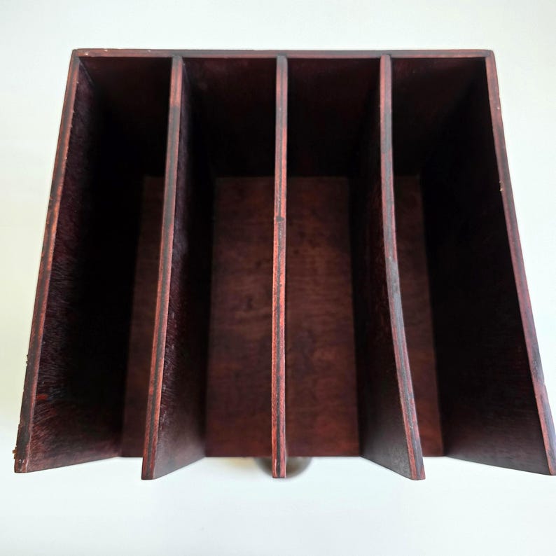 May include: A wooden desk organizer with five vertical compartments. The organizer is made of dark brown wood and has a trapezoidal shape. The compartments are separated by thin wooden dividers, creating a storage solution for office supplies or documents.