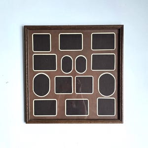 May include: A square wooden picture frame featuring a brown mat board with twelve cutouts for photographs. The arrangement includes four rectangular, four square, two oval, and two smaller vertical oval openings, all outlined in white.