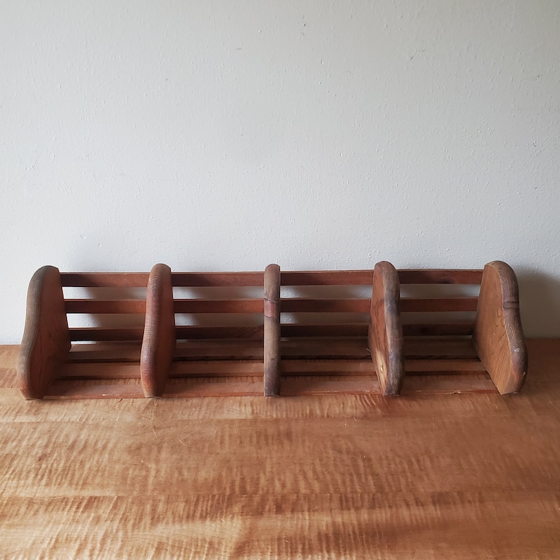 May include: A wooden shelf unit with four compartments, each with a slatted front. The shelf is made of natural wood with a rustic finish.