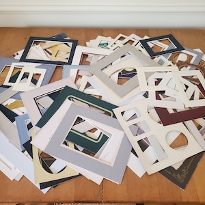 May include: A large pile of white, cream, and gray picture frames of various sizes and shapes. The frames are made of cardboard and have a simple design.
