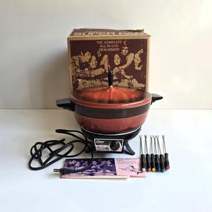 May include: An Oster Super Pan electric skillet with a burnt orange and brown finish, a matching lid, and a black base with a temperature control dial. Includes six fondue forks with colored tips, a power cord, an instruction manual, and the original box.