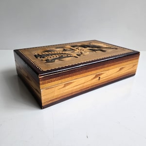 May include: A rectangular wooden box with a carved floral design on the lid. The box features a keyhole and is made of light and dark brown wood. The lid has a scalloped edge.
