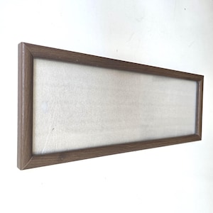 May include: A rectangular wooden picture frame with a light-colored interior. The frame is a medium brown color and has a simple, clean design. The frame is empty, ready for a photo or artwork.