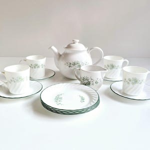 May include: A white tea set with a green floral pattern. The set includes a teapot, creamer, four cups, and four saucers.