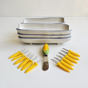 May include: A set of ceramic serving dishes with a blue rim, stacked, and a collection of yellow corn-shaped corn holders with metal prongs. A butter knife with a corn-shaped handle is also included.