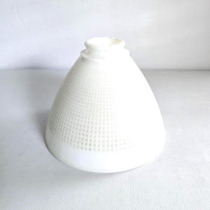 May include: A white glass lamp shade with a conical shape and a textured grid pattern covering the exterior surface. The shade features a circular opening at the top with a raised rim, designed for attachment to a light fixture base.