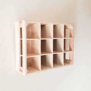 May include: A wooden shelf unit with 12 square compartments. The shelf is made of light wood and has a natural finish.