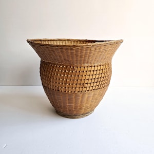 May include: A large, brown wicker basket with a wide, rounded top and a narrow base. The basket is woven with a tight, intricate pattern.