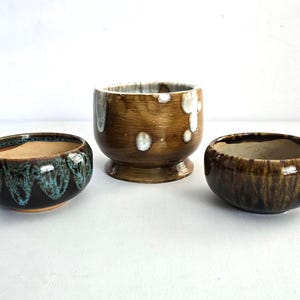 May include: Three ceramic bowls in varying sizes and designs. The bowls feature brown, teal, and white glaze patterns. The largest bowl has a pedestal base. The bowls are suitable for decorative or functional use.