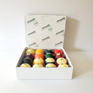 May include: A set of 15 Aramith billiard balls in a white box. The balls are numbered 1 through 15 and are arranged in a grid pattern. The balls are a variety of colors, including red, yellow, blue, green, and black.