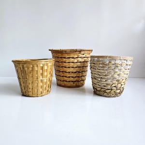 May include: Three woven baskets of varying sizes and designs. The basket on the left is made of light-colored bamboo, the middle basket has dark brown horizontal stripes, and the right basket is made of light-colored woven material.