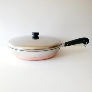 May include: A silver and copper cookware set with a black handle and lid. The lid has a black knob.