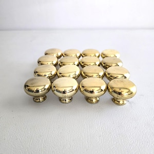 May include: A collection of sixteen shiny, gold-colored cabinet knobs. Each knob has a rounded top and a decorative base. The knobs are arranged in a grid pattern, suggesting they are ready for installation on furniture.