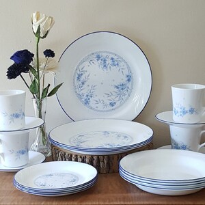 May include: A set of white Corelle dinnerware with a blue floral pattern. The set includes plates, bowls, and mugs.