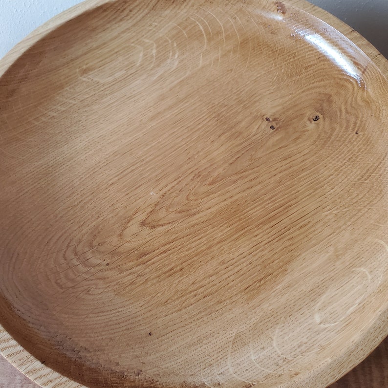 K&ouml;nnte beinhalten: Eine handgefertigte Holzschale mit quadratischer Form und abgerundeten Ecken. Die Schale besteht aus hellem Holz mit sichtbaren Maserungsmustern und einer gl&auml;nzenden Oberfl&auml;che. Der Innenraum ist glatt und scheint lebensmittelecht zu sein.