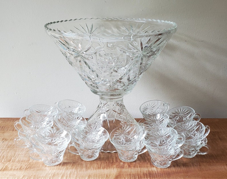 May include: A large clear glass punch bowl with a starburst pattern and 10 matching cups. The bowl has a pedestal base.