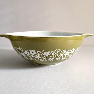 May include: Olive green mixing bowl with white floral pattern. The bowl has a white interior and two handles. A vintage kitchenware item.