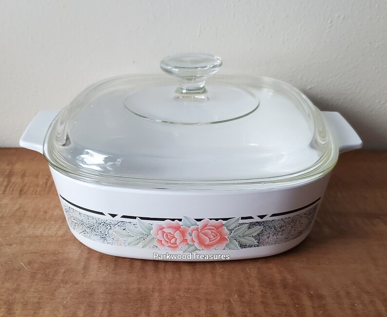 May include: White square baking dish with a glass lid. The dish has a floral design with pink roses and green leaves on a gray background. The text "Parkwood Treasures" is printed on the bottom of the dish.