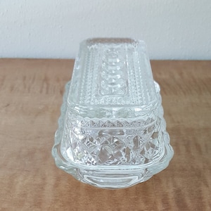May include: A clear glass butter dish with a decorative, diamond-shaped pattern. The dish has a lid and a rectangular base.