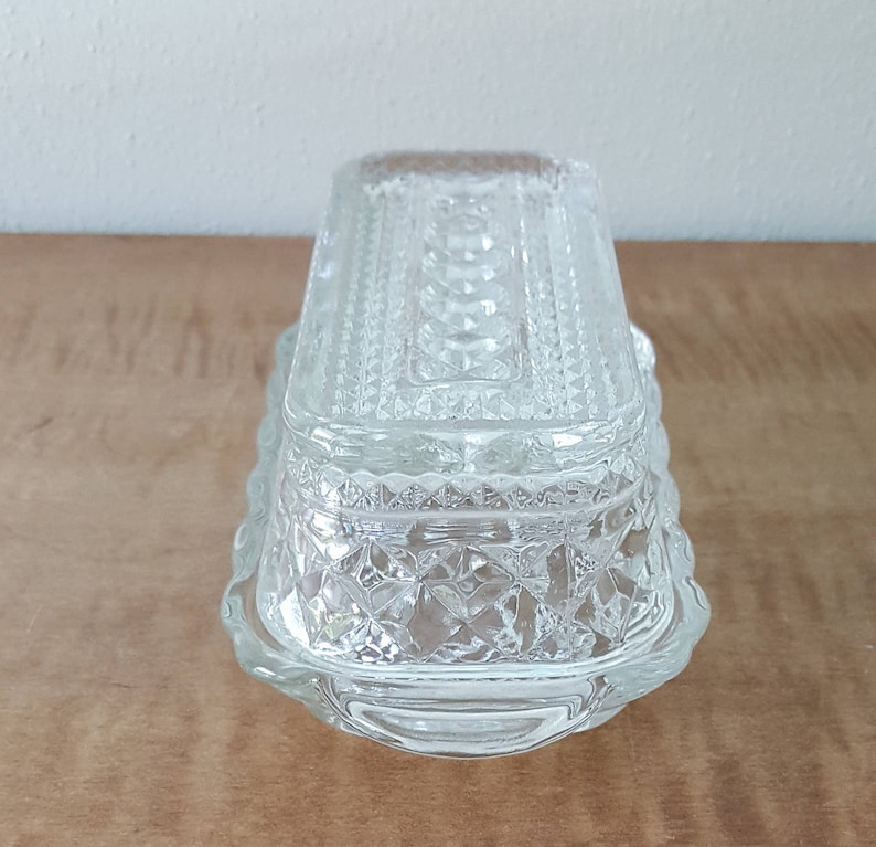 May include: A clear glass butter dish with a decorative, diamond-shaped pattern. The dish has a lid and a rectangular base.