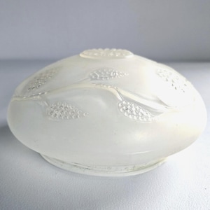 May include: A frosted glass lampshade with a rounded shape and a decorative floral pattern. The shade is off-white and features a textured surface with raised floral designs. The base has a slight lip, and the top has a small, textured design.