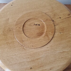 K&ouml;nnte beinhalten: Runder Servierteller aus hellbraunem Holz mit einem kreisf&ouml;rmigen, vertieften Bereich in der Mitte. Das Tablett hat eine nat&uuml;rliche Holzmaserung und die Initialen "JHA" sind in der Mitte sichtbar.