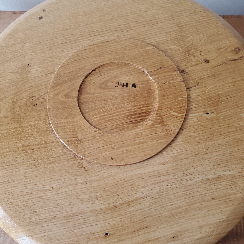 K&ouml;nnte beinhalten: Runder Servierteller aus hellbraunem Holz mit einem kreisf&ouml;rmigen, vertieften Bereich in der Mitte. Das Tablett hat eine nat&uuml;rliche Holzmaserung und die Initialen "JHA" sind in der Mitte sichtbar.