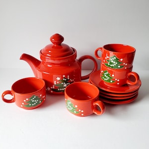 May include: A red ceramic teapot and four teacups with matching saucers. The teapot and cups are decorated with green Christmas trees and white stars.