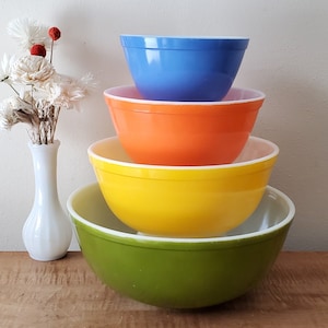 May include: A set of four nesting mixing bowls in green, yellow, orange, and blue. The bowls are made of glass and have a vintage look.